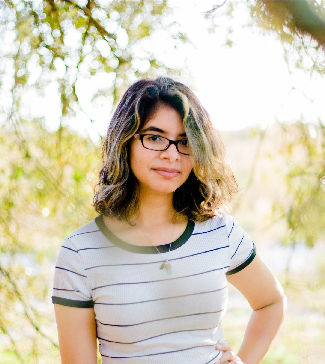 Head shot photo of Young adult Hispanic American woman with outdoor greenery background.