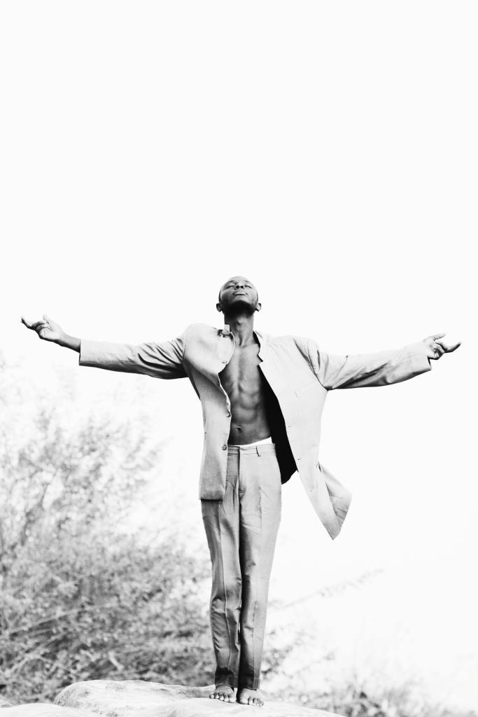 Black and white photo of a man standing on a rock with his hands stretched out to both sides and his head back looking at the sky
